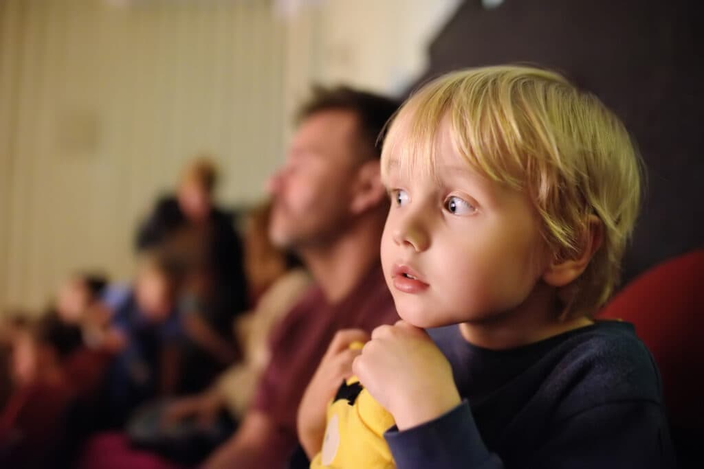 Cute little boy with his father watching cartoon movie in the cinema or performance in viewer hall of theatre. Leisure entertainment for family with kids. Cultural event for children.