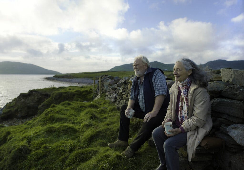 vanha mies ja vanha nainen istuvat penkillä ja katsovat merta