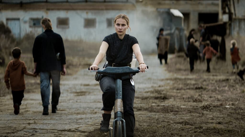 Nainen ajaa sähköpyörällä ränsistyneen kylän keskustan läpi